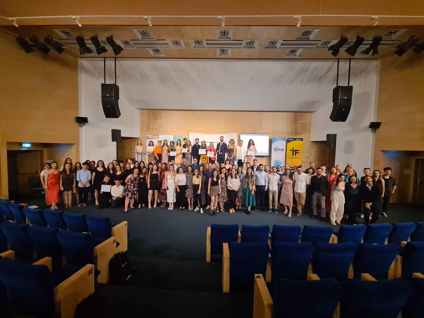 Fotografie de grup cu participanții adunați în fața scenei unei săli de conferințe